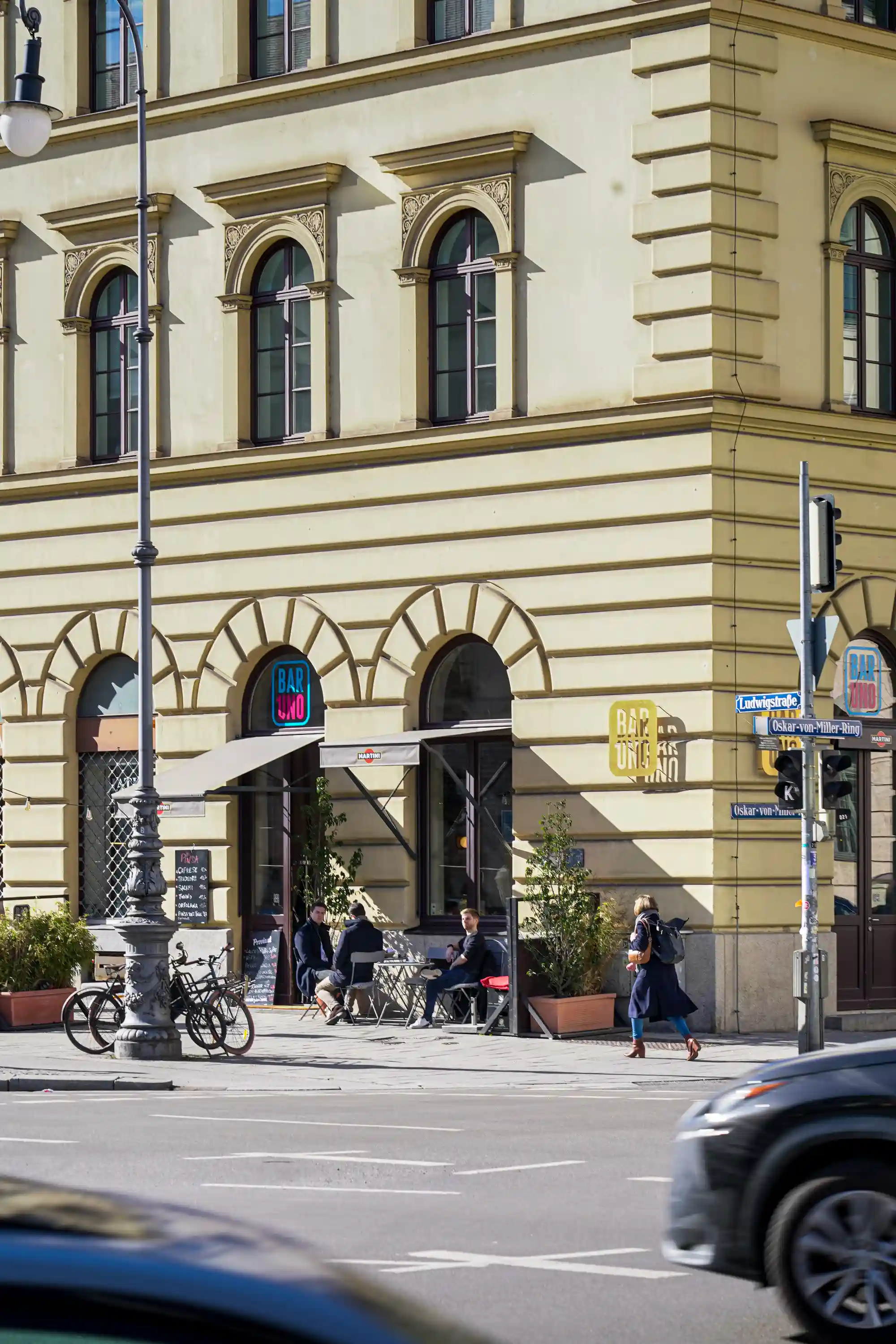 Kunden frühstücken im sonnigen Außenbereich der Bar unter Markisen